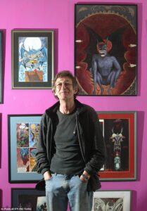 Alan Grant in front of posters of comics characters he has written